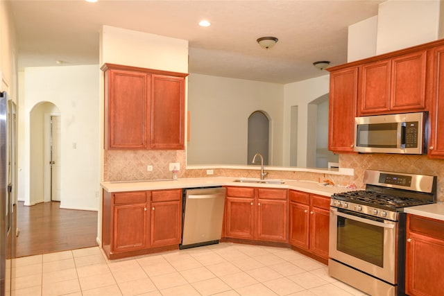 kitchen featuring arched walkways, decorative backsplash, stainless steel appliances, light countertops, and a sink