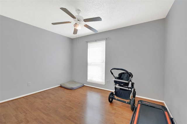 workout room featuring a textured ceiling, wood finished floors, a ceiling fan, and baseboards