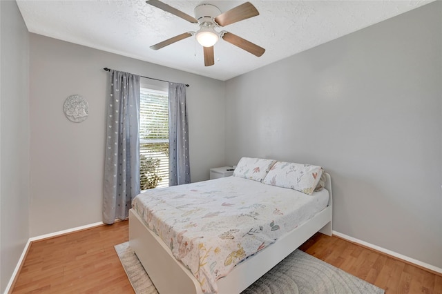 bedroom with light wood-style floors, a textured ceiling, and baseboards