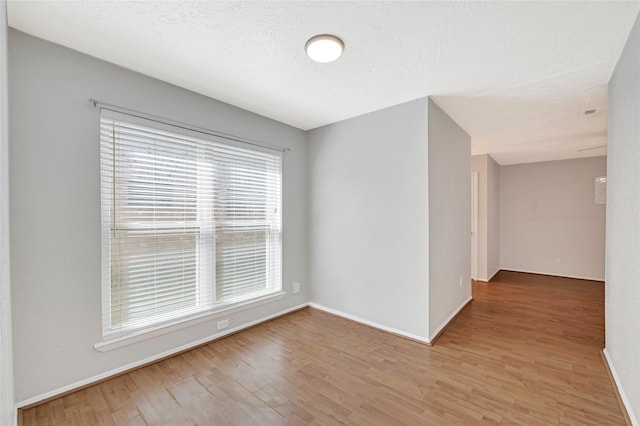 empty room featuring light wood finished floors, baseboards, and a textured ceiling