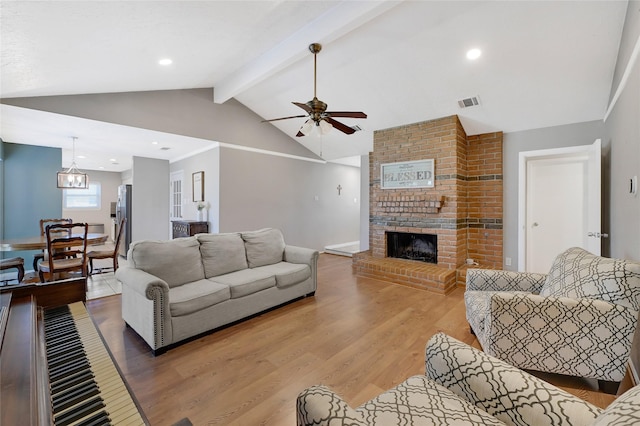 living room featuring lofted ceiling with beams, light wood-style flooring, ceiling fan with notable chandelier, a fireplace, and visible vents