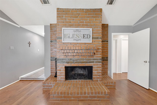 unfurnished living room featuring vaulted ceiling, a brick fireplace, wood finished floors, and visible vents