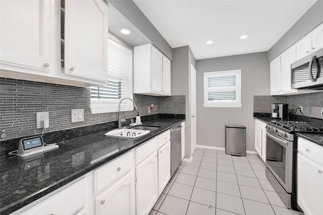 kitchen featuring stainless steel appliances, dark stone counters, white cabinetry, and a sink