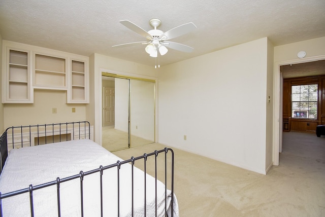 bedroom featuring a ceiling fan, a textured ceiling, a closet, baseboards, and light colored carpet