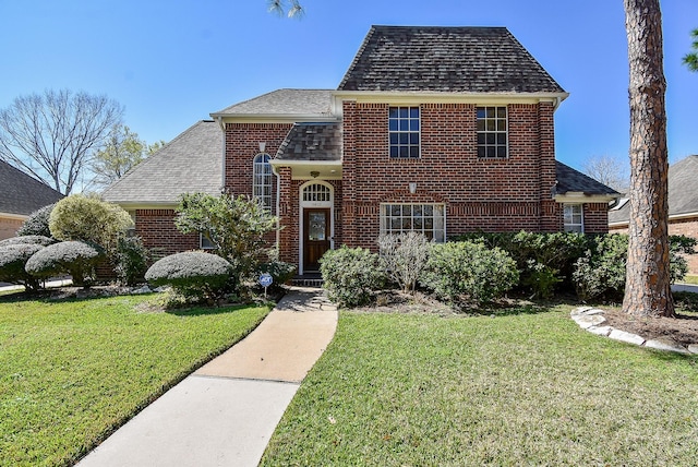 traditional-style home featuring brick siding, a front yard, and a shingled roof