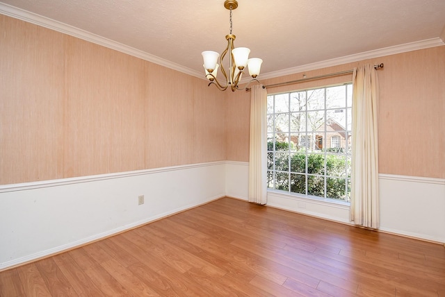 spare room with a notable chandelier, plenty of natural light, and wood finished floors