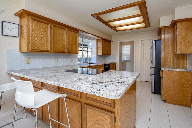 kitchen featuring wallpapered walls, brown cabinets, a peninsula, light tile patterned flooring, and black appliances