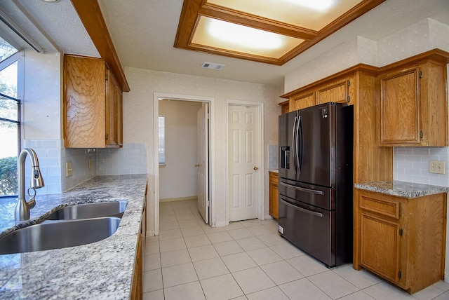 kitchen with brown cabinetry, black fridge with ice dispenser, light tile patterned flooring, and a sink