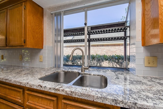 kitchen featuring brown cabinetry, backsplash, light stone countertops, and a sink