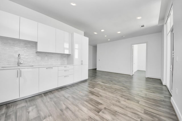 kitchen featuring light wood finished floors, a sink, light countertops, white cabinetry, and backsplash