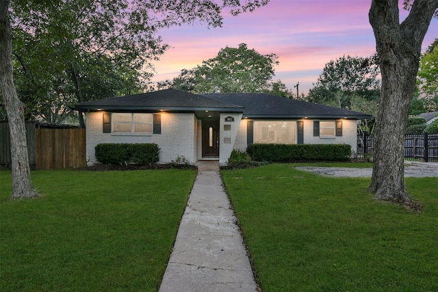 ranch-style house with brick siding, fence, and a lawn