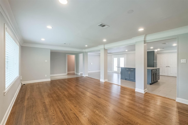 unfurnished living room featuring visible vents, light wood-style flooring, crown molding, and ornate columns