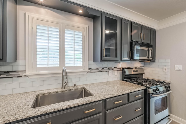 kitchen featuring decorative backsplash, a sink, appliances with stainless steel finishes, glass insert cabinets, and light stone countertops