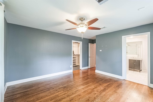 unfurnished bedroom with visible vents, ensuite bathroom, baseboards, and wood finished floors