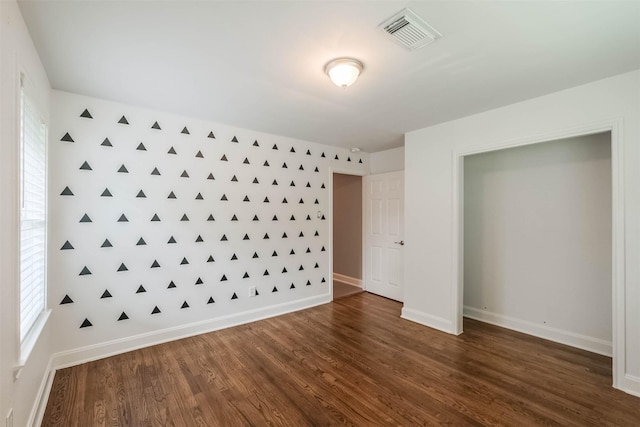 unfurnished bedroom featuring visible vents, baseboards, dark wood finished floors, and an accent wall