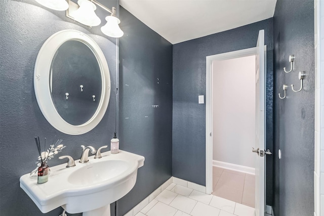 bathroom featuring tile patterned floors, a textured wall, baseboards, and a sink