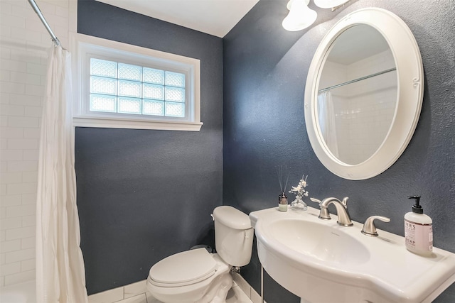 full bathroom featuring tiled shower, toilet, a textured wall, and a sink