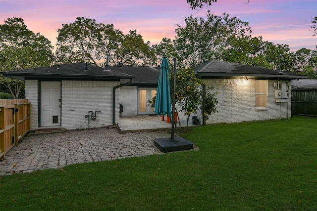 back of property at dusk with a patio, a yard, fence, and brick siding