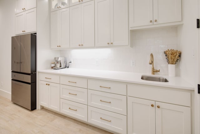 kitchen with white cabinets, freestanding refrigerator, a sink, light countertops, and backsplash