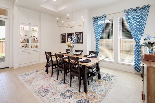 dining room featuring a chandelier, a tray ceiling, light wood finished floors, and a wealth of natural light