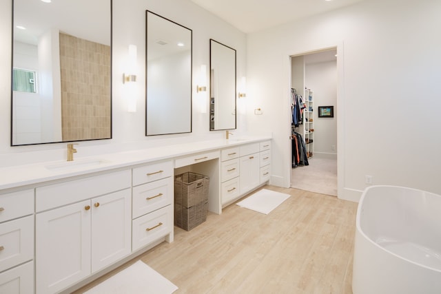 bathroom with double vanity, a sink, wood finished floors, a freestanding tub, and baseboards