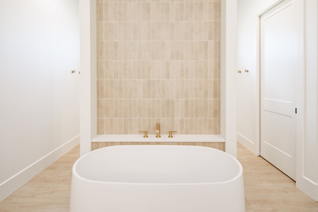 bathroom featuring a freestanding tub, baseboards, and wood finished floors