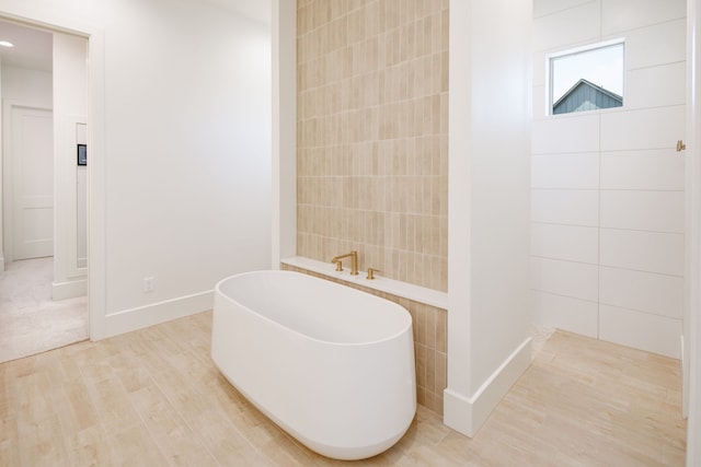 bathroom with baseboards, a freestanding bath, and wood finished floors