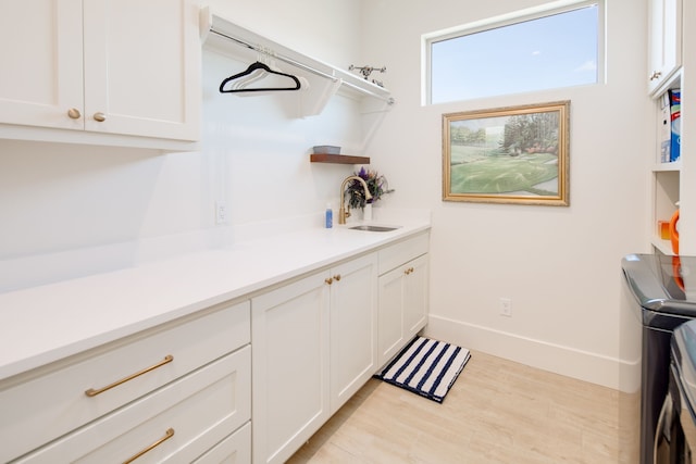 laundry area featuring a sink, baseboards, independent washer and dryer, cabinet space, and light wood finished floors