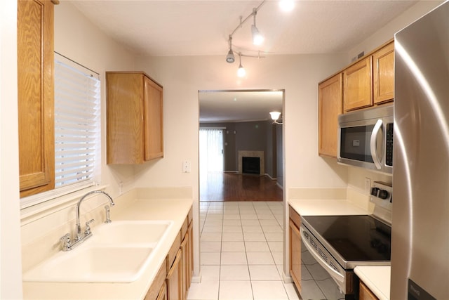 kitchen featuring light tile patterned floors, stainless steel appliances, light countertops, a fireplace, and a sink