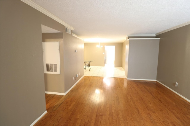 spare room featuring a textured ceiling, wood finished floors, visible vents, baseboards, and ornamental molding