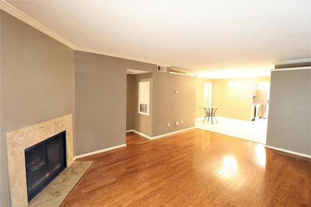 unfurnished living room with wood finished floors, visible vents, baseboards, a high end fireplace, and crown molding