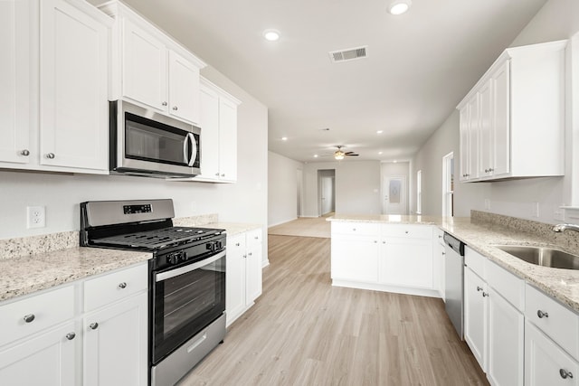 kitchen with light wood finished floors, visible vents, a peninsula, stainless steel appliances, and a sink