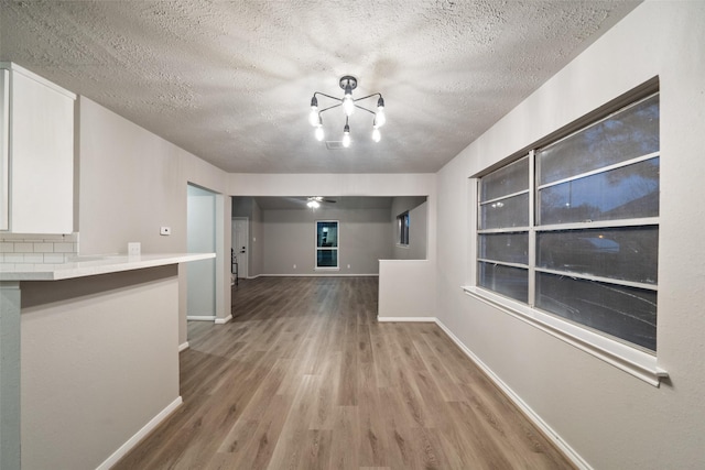 interior space with a notable chandelier, a textured ceiling, baseboards, and wood finished floors