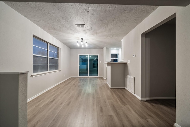 unfurnished living room featuring baseboards, a textured ceiling, visible vents, and wood finished floors