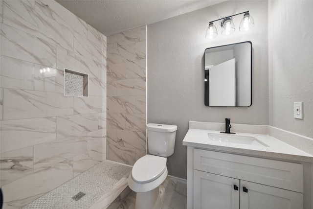 bathroom featuring marble finish floor, a textured wall, toilet, vanity, and tiled shower