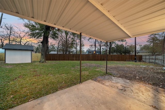 yard at dusk featuring a storage shed, a fenced backyard, an outdoor structure, and a patio