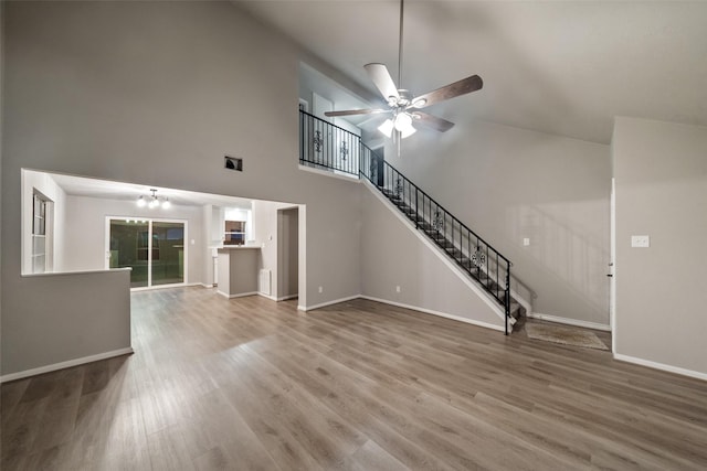 unfurnished living room with baseboards, stairway, wood finished floors, and ceiling fan with notable chandelier