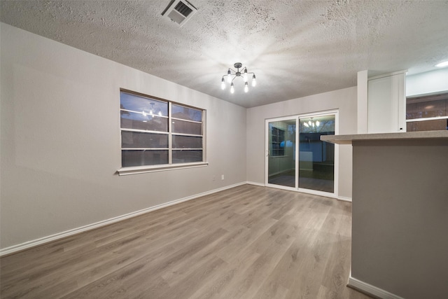 unfurnished room featuring baseboards, a textured ceiling, visible vents, and wood finished floors