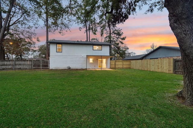 back of property at dusk with brick siding, a fenced backyard, and a yard