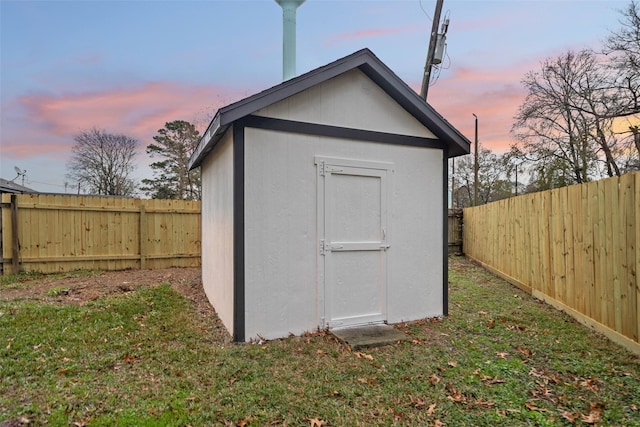 outdoor structure at dusk with an outbuilding, a lawn, and a fenced backyard