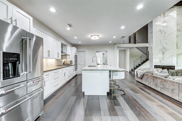 kitchen featuring wall chimney exhaust hood, high quality fridge, a breakfast bar, open floor plan, and a sink