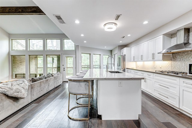 kitchen featuring open floor plan, wall chimney exhaust hood, a sink, and visible vents