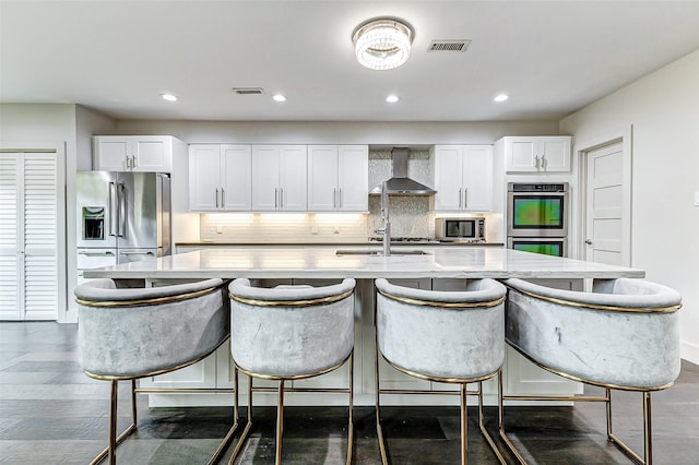 kitchen featuring visible vents, wall chimney range hood, backsplash, and appliances with stainless steel finishes