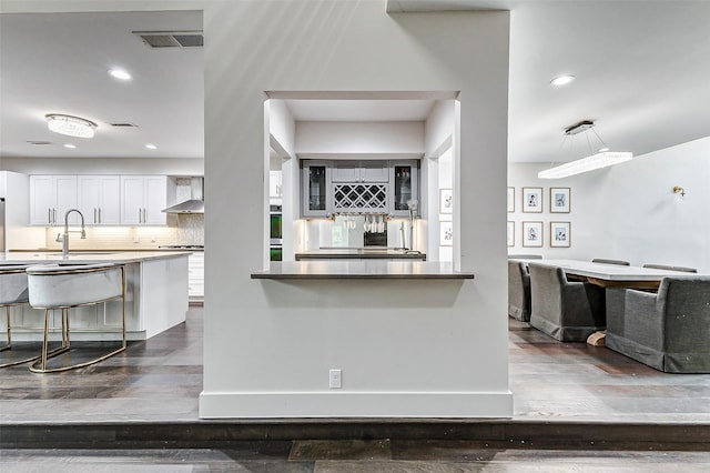 kitchen with wall chimney exhaust hood, a breakfast bar area, tasteful backsplash, and dark wood-type flooring