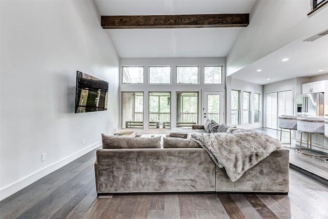 living area with dark wood-type flooring, beamed ceiling, a high ceiling, and baseboards