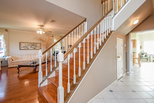 stairs featuring wood finished floors, a ceiling fan, visible vents, baseboards, and a high ceiling