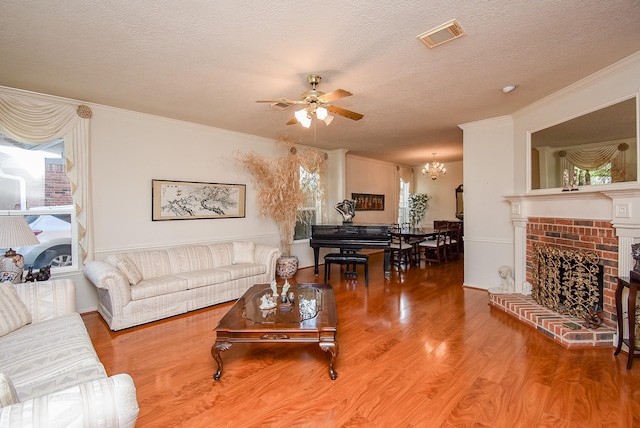 living area with wood finished floors, visible vents, a fireplace, ornamental molding, and a textured ceiling