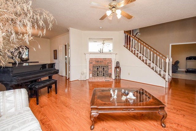 living room featuring stairway, a brick fireplace, a ceiling fan, and wood finished floors