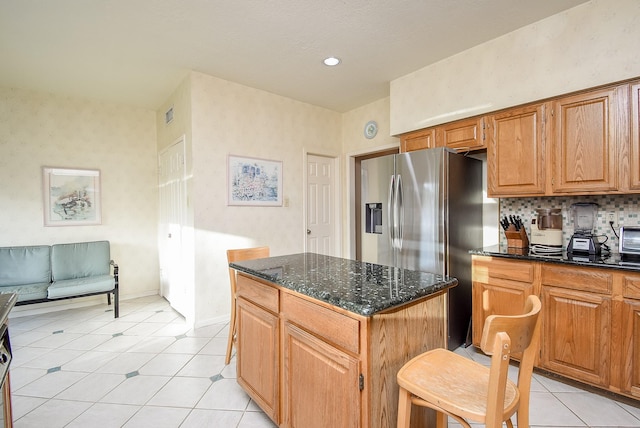 kitchen with backsplash, a kitchen island, baseboards, dark stone countertops, and light tile patterned flooring