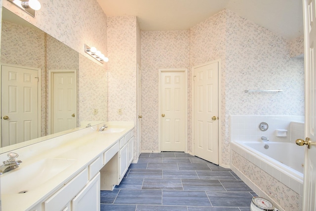 full bath featuring wallpapered walls, a garden tub, double vanity, and a sink